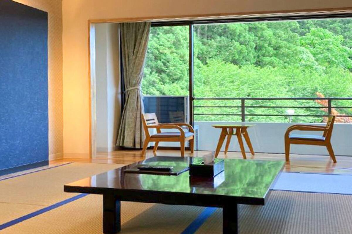 Una habitación con un ventanal grande, un televisor de pantalla plana, una mesa de madera y dos sillas.