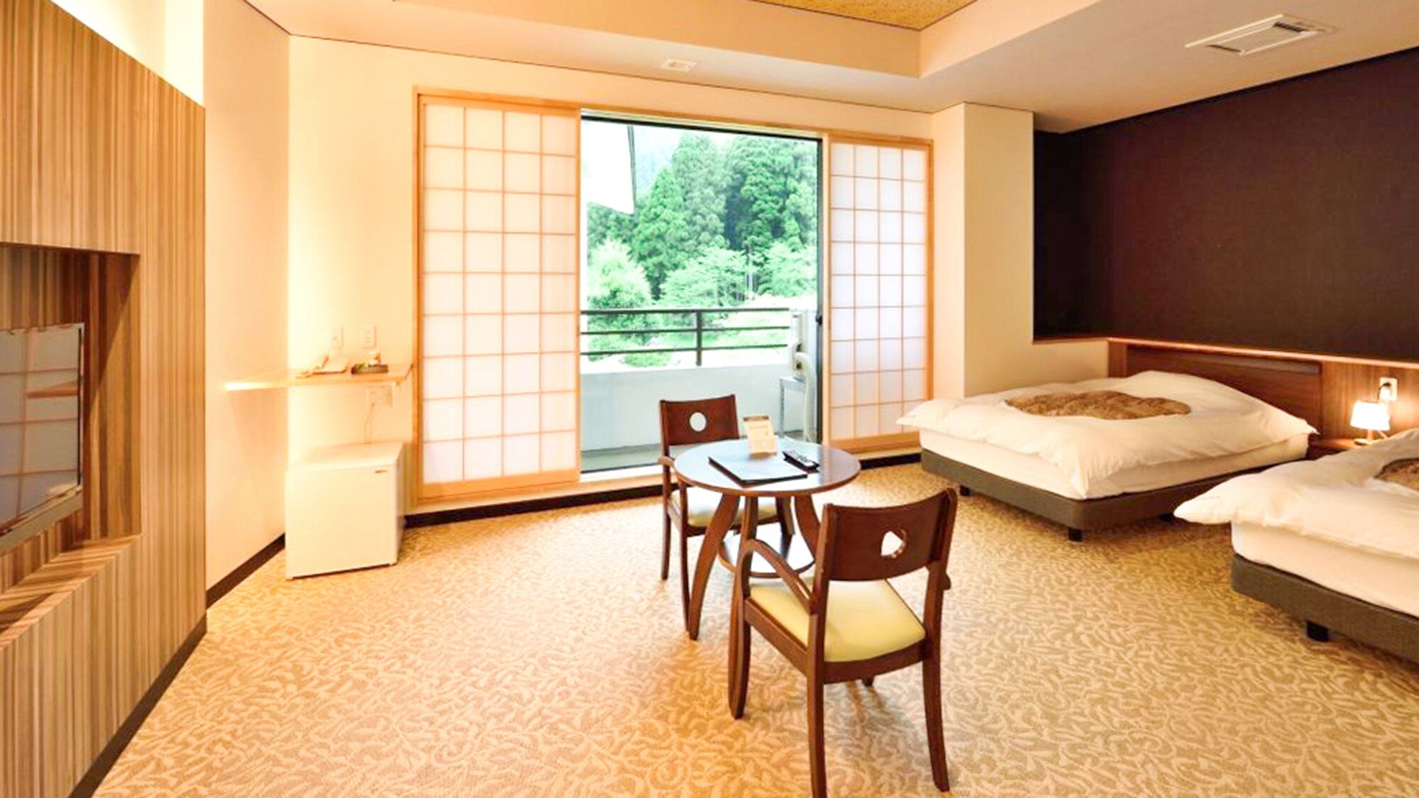 A hotel room with a traditional Japanese aesthetic, featuring tatami flooring, a low table with chairs, a bed with a headboard, and a sliding glass door leading to a balcony.