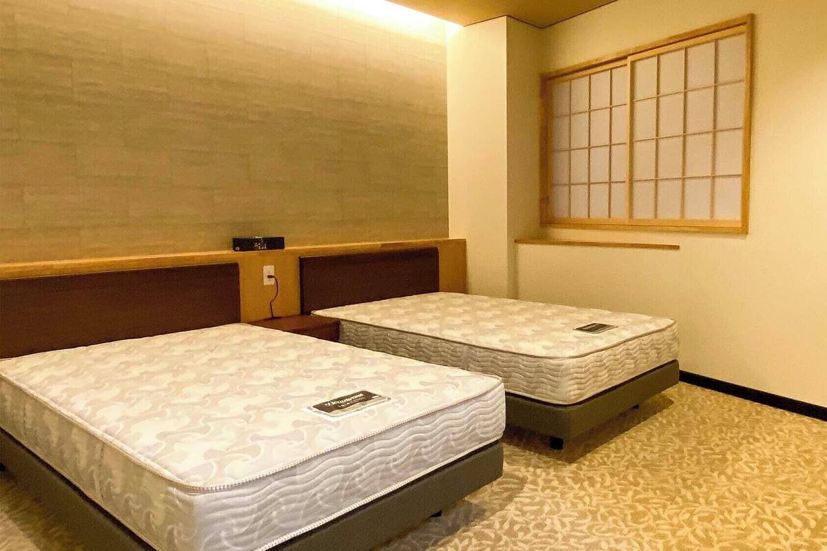 Una habitación con dos camas, una ventana con diseño de cuadrícula y un enchufe en la pared.