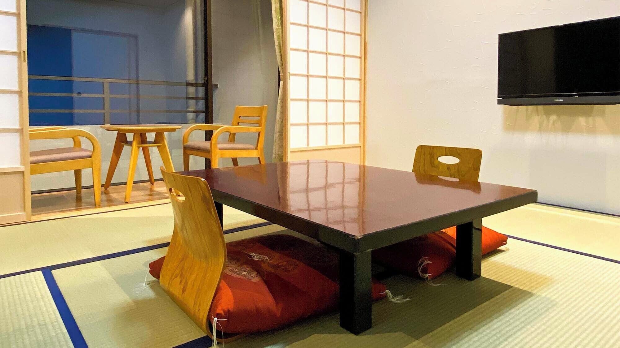 A traditional Japanese room with tatami flooring, a low table, wooden chairs, and a television.