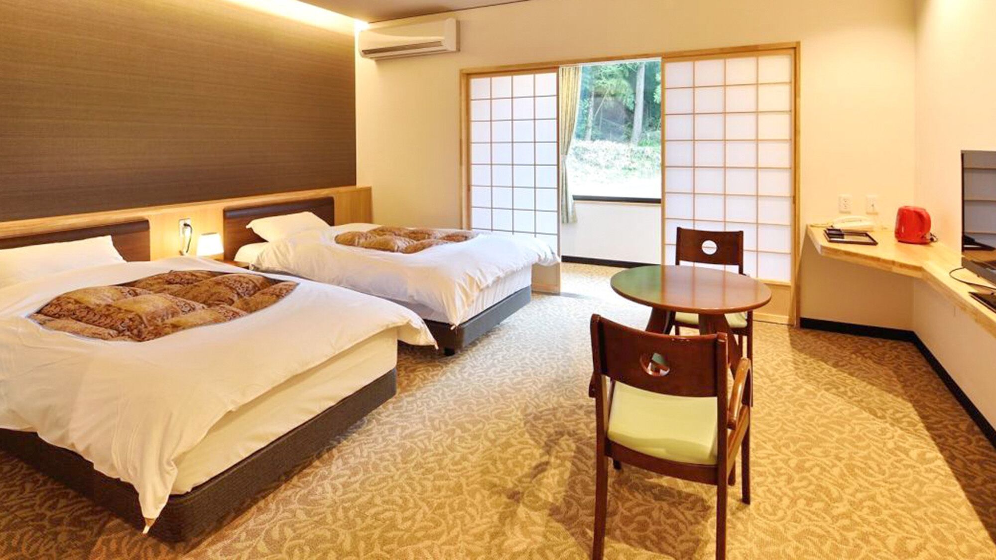 A hotel room with two beds, a small table, a chair, and a view of the outdoors through a sliding door.