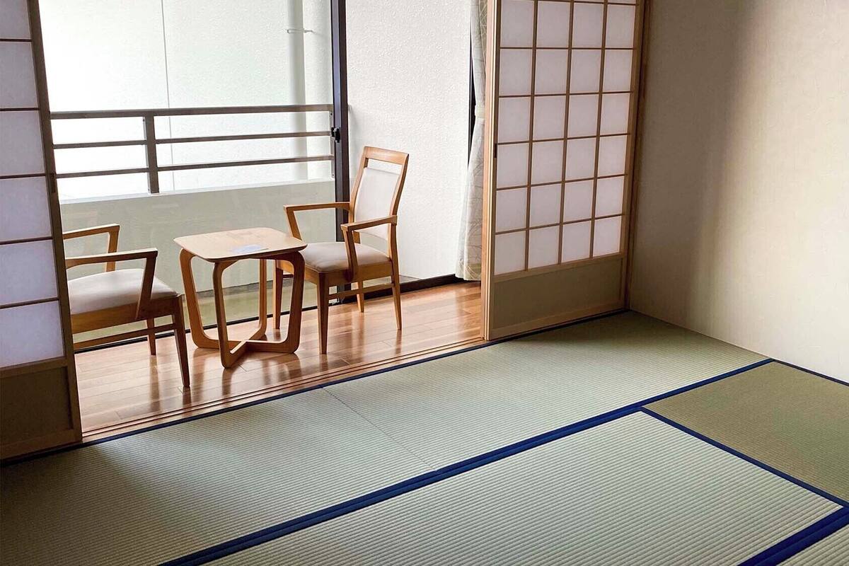 Una habitación tradicional japonesa con suelo de tatami, una puerta corredera shoji y una mesa baja con sillas.