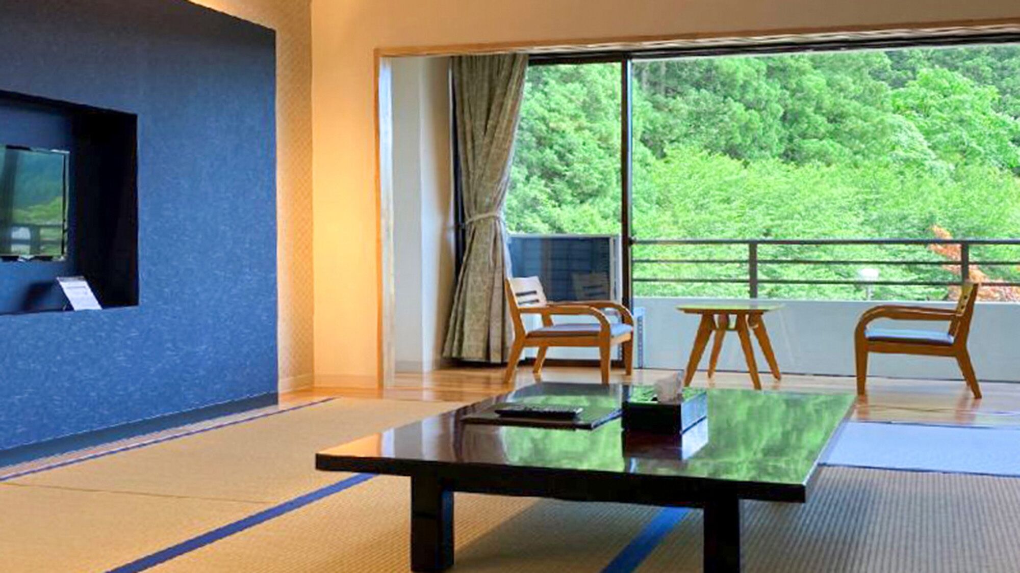 A room with a large window, a flat-screen TV, a wooden table, and two wooden chairs.