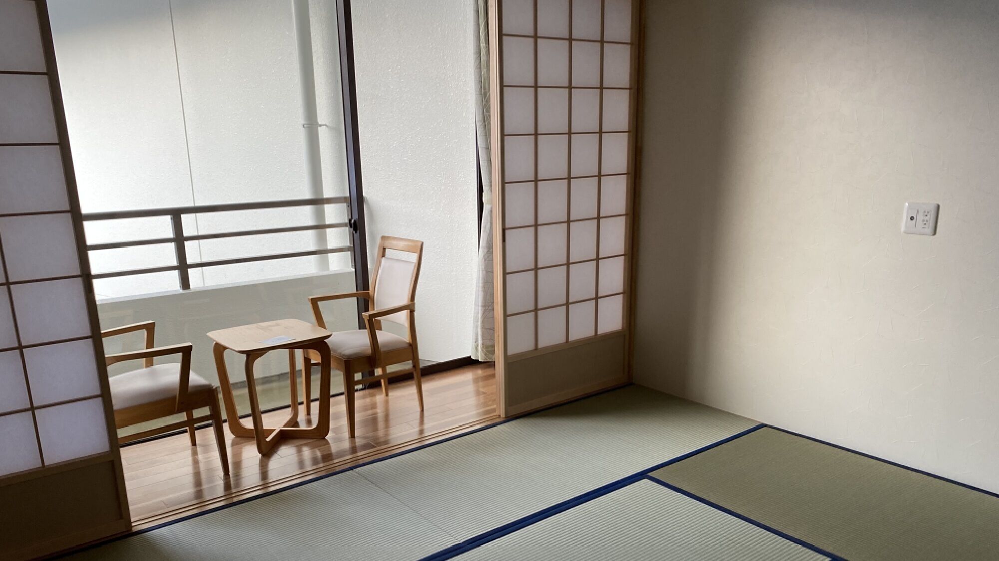 A traditional Japanese room with tatami flooring, a sliding shoji screen door, and a low wooden table with chairs.