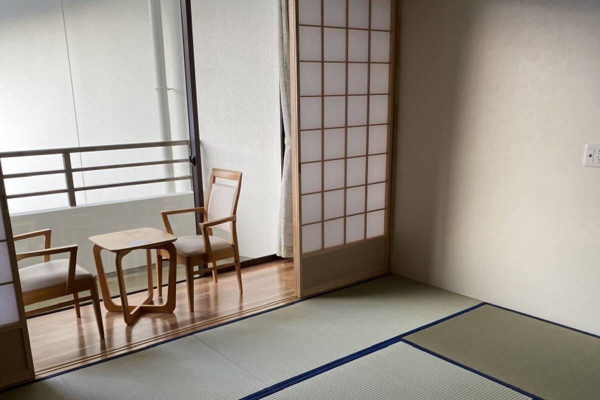 Una habitación japonesa tradicional con suelo de tatami, una puerta corredera estilo shoji y una mesa de madera baja con sillas.