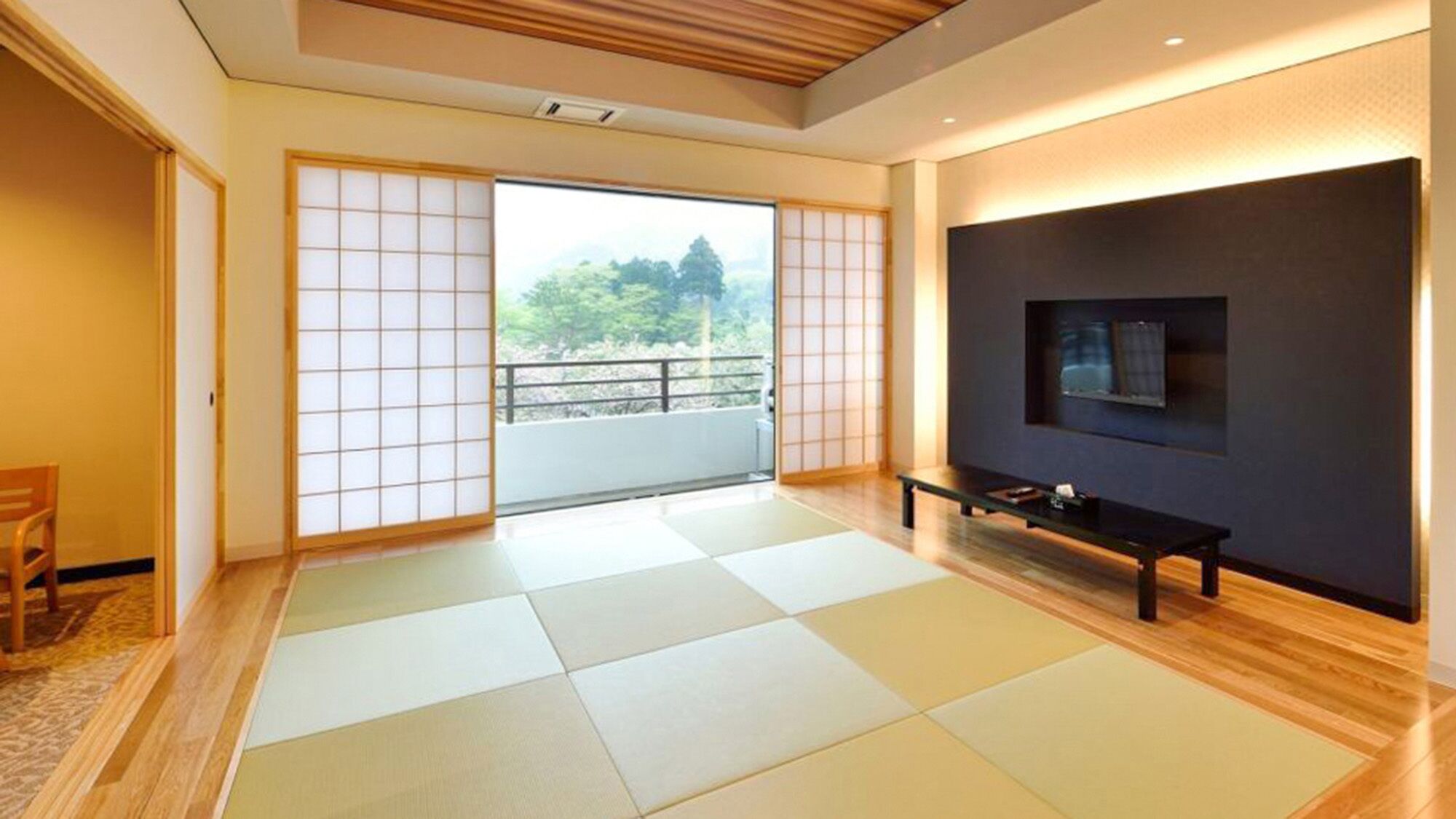 A room with tatami mats, a sliding door to a balcony, a TV mounted on the wall, and a bench.