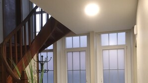 Un escalier avec des rampes en bois, un sol à carreaux et un radiateur près d’une fenêtre.