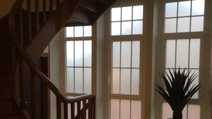 Une pièce spacieuse avec un escalier en bois, de grandes fenêtres et une plante en pot.