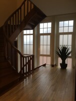 Una habitación amplia con escaleras de madera, ventanas grandes y una planta en maceta.