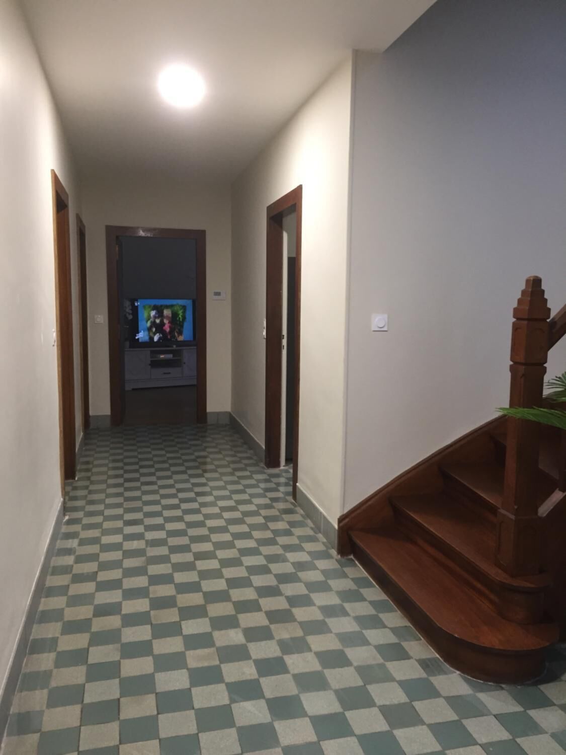 A hallway with a checkered floor, wooden doors, and a staircase with a wooden handrail.