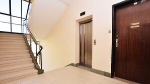 Eine Treppe mit Metallgeländer, eine Holztür und ein Aufzug in einer gefliesten Diele.