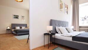 Ein modernes Hotelzimmer mit einem großen Bett, einem kleineren Bett, einem Nachttisch mit Lampe, einem Fenster mit Vorhängen und Bildern an den Wänden.