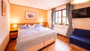 Un dormitorio con cama, mesitas de noche, televisor, ventana con cortinas y sofá.