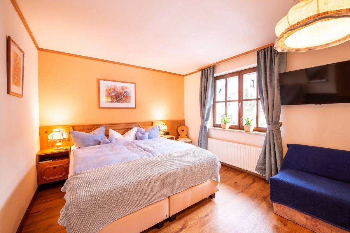 Ein Schlafzimmer mit Bett, Nachttischen, einem Fernseher, einem Fenster mit Vorhängen und einem Sofa.
