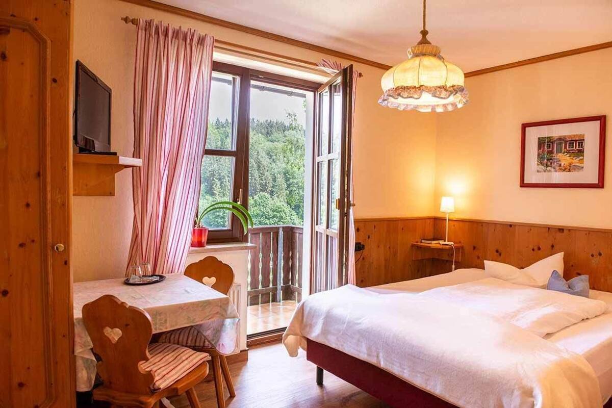 Ein Schlafzimmer mit Bett, Schreibtisch mit Stuhl, Fenster mit Vorhängen, Nachttisch mit Lampe und einem gerahmten Bild an der Wand.