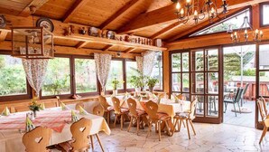 Un interior de madera con mesas y sillas, ventanas amplias y un candelabro.
