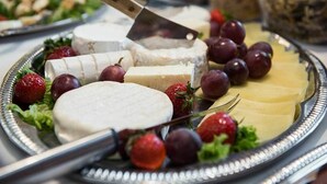 Una tabla de quesos con diferentes tipos de queso, uvas y fresas sobre una bandeja de plata.