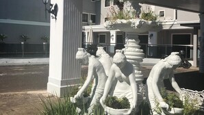 Un edificio con fachada blanca, una fuente con estatuas y un área de entrada pavimentada.