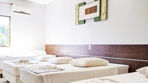 Habitación de hotel con tres camas individuales, un ventanal grande y un aire acondicionado instalado en la pared.