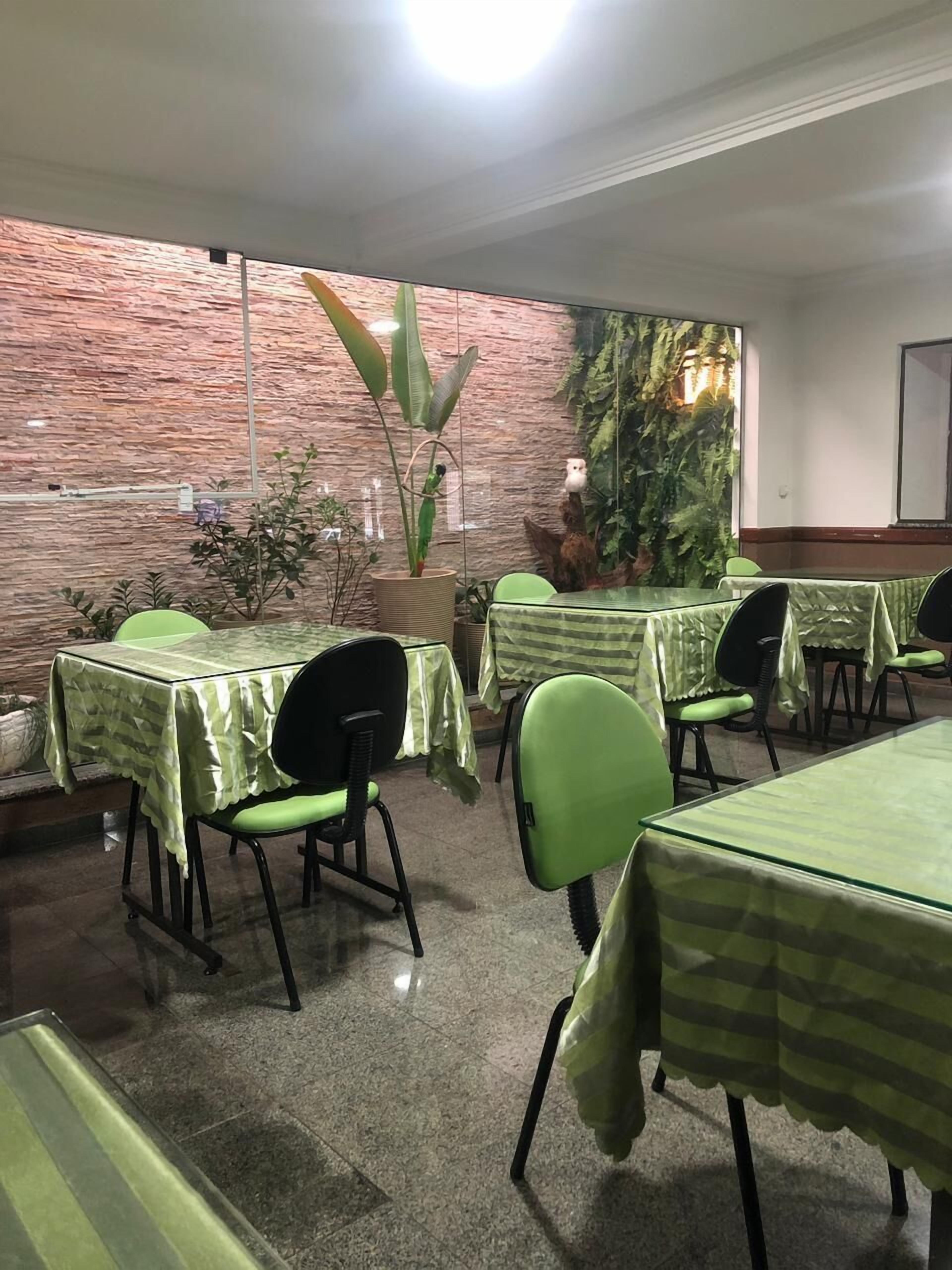 A restaurant with green-striped tablecloths and chairs, a brick wall, and indoor plants.
