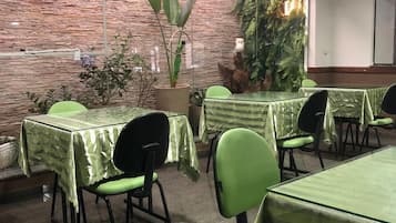 A restaurant with green-striped tablecloths and chairs, a brick wall, and indoor plants.