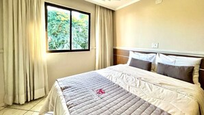 Una habitación de hotel con cama, cortinas, ventana y toma de corriente.