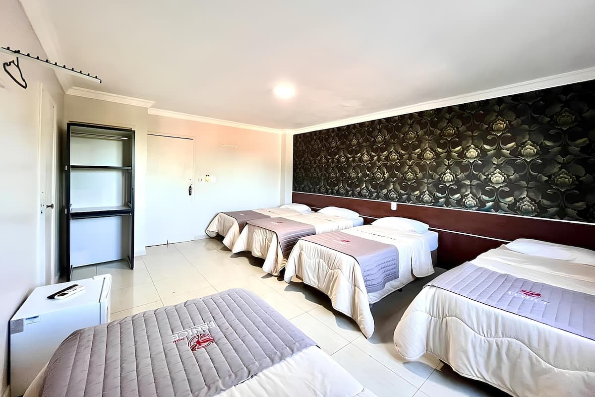 A hotel room with four beds, a wardrobe, a small desk, and a decorative wall.