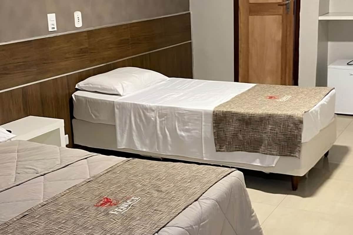 A hotel room with two beds, a wooden headboard, a small white bedside table, and a white wardrobe.