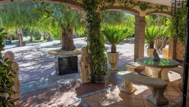 Ein überdachter Patio-Bereich mit Steinbänken, Blumentöpfen und einer Statue.