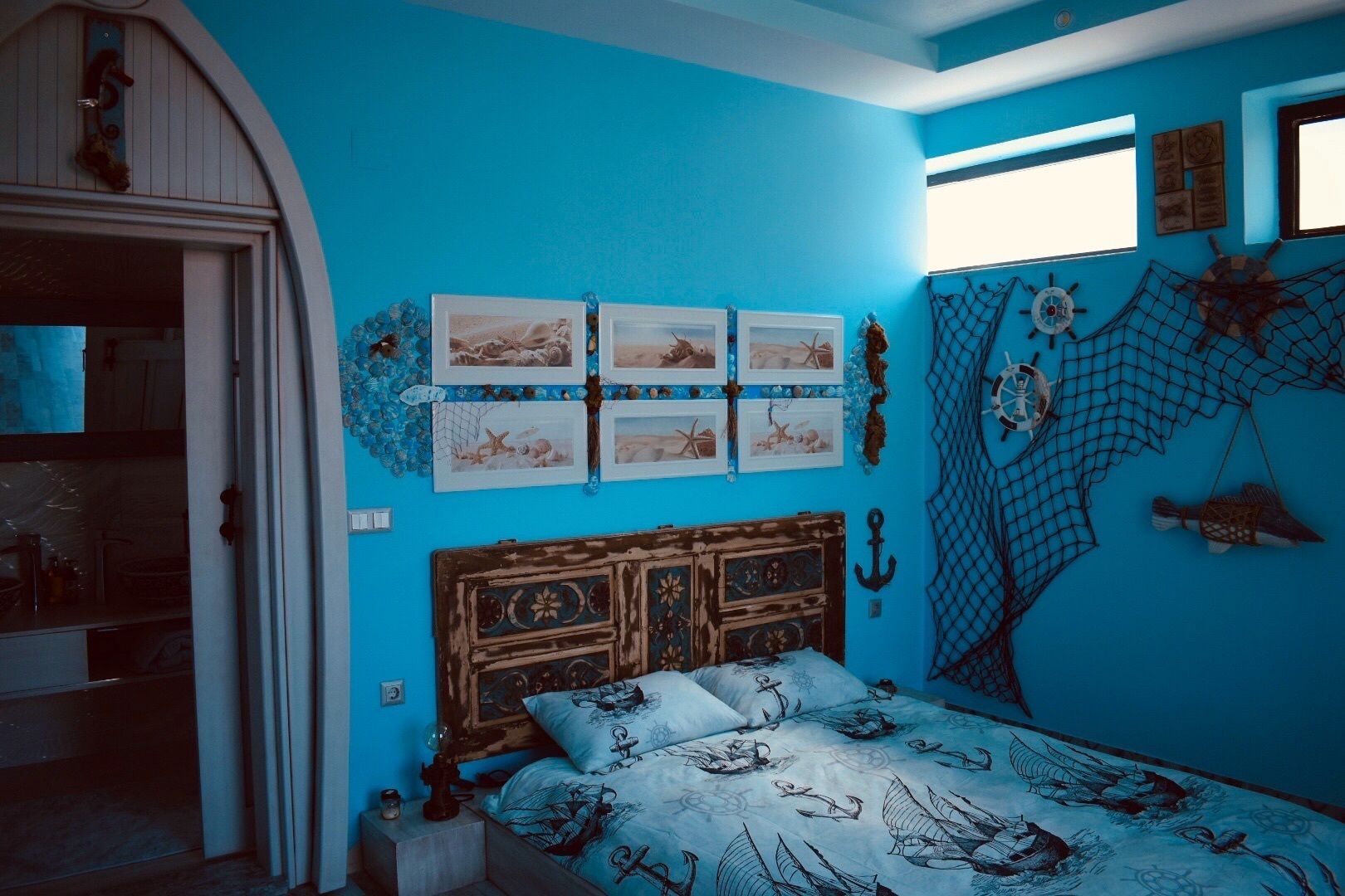 Un dormitorio con una pared azul, una cama de madera con temática náutica y una ventana con vistas.