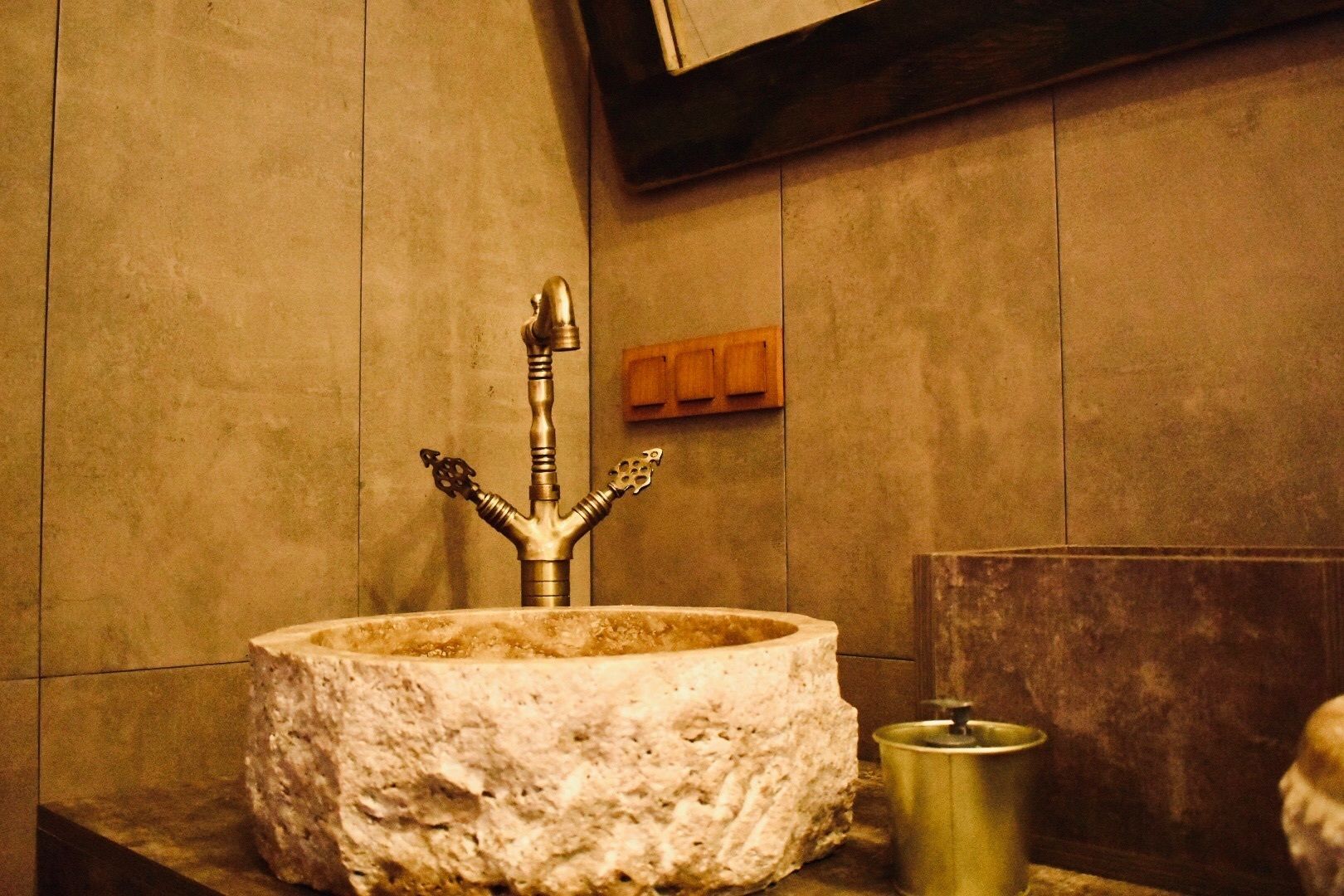 A stone sink with a unique faucet design in a room with wooden walls and a wooden cabinet.