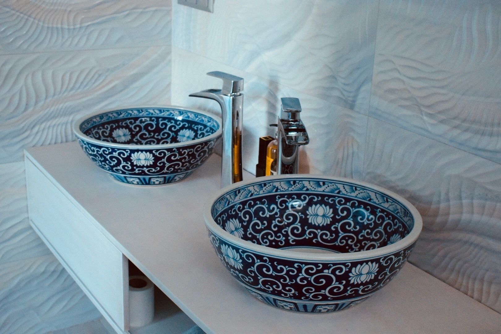 A bathroom with two ornate bowls on a white vanity, a modern faucet, and a textured wall.