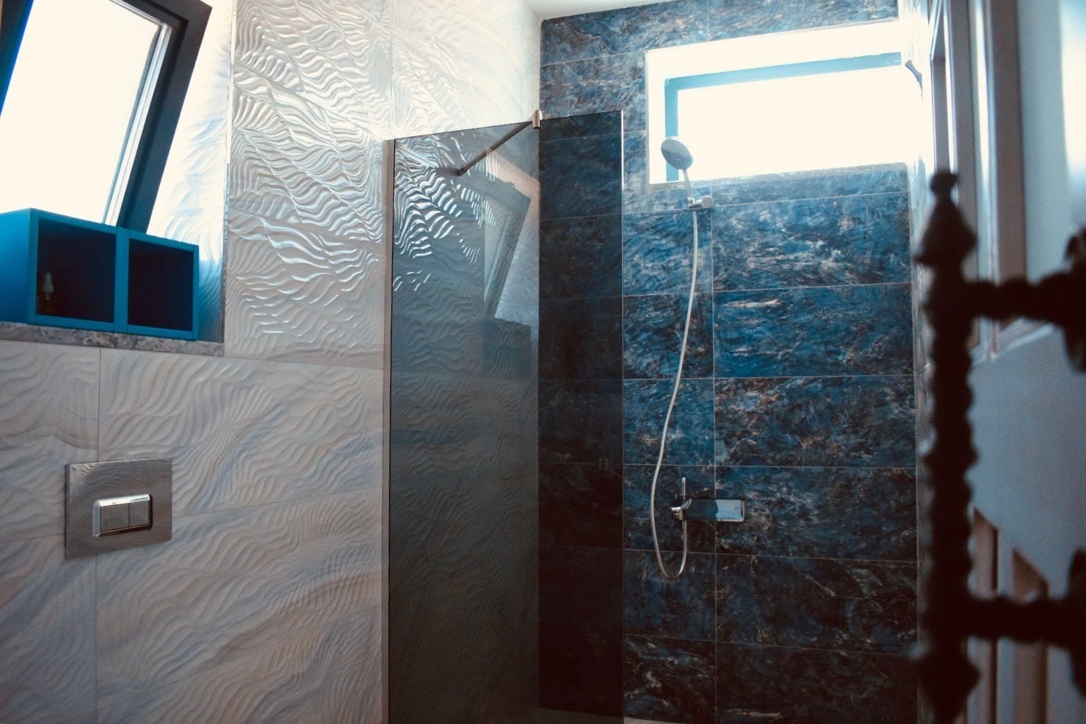 Un baño moderno con cabina de ducha de cristal, pared de mármol y ventana que proporciona luz natural.