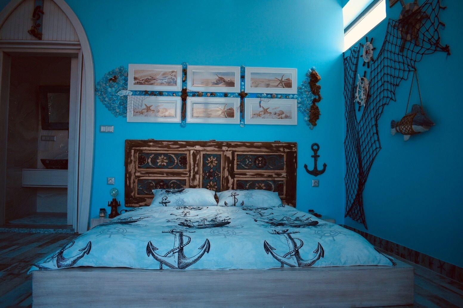 Een slaapkamer met een blauwe wand, een houten bedframe en beddengoed met een nautisch thema.