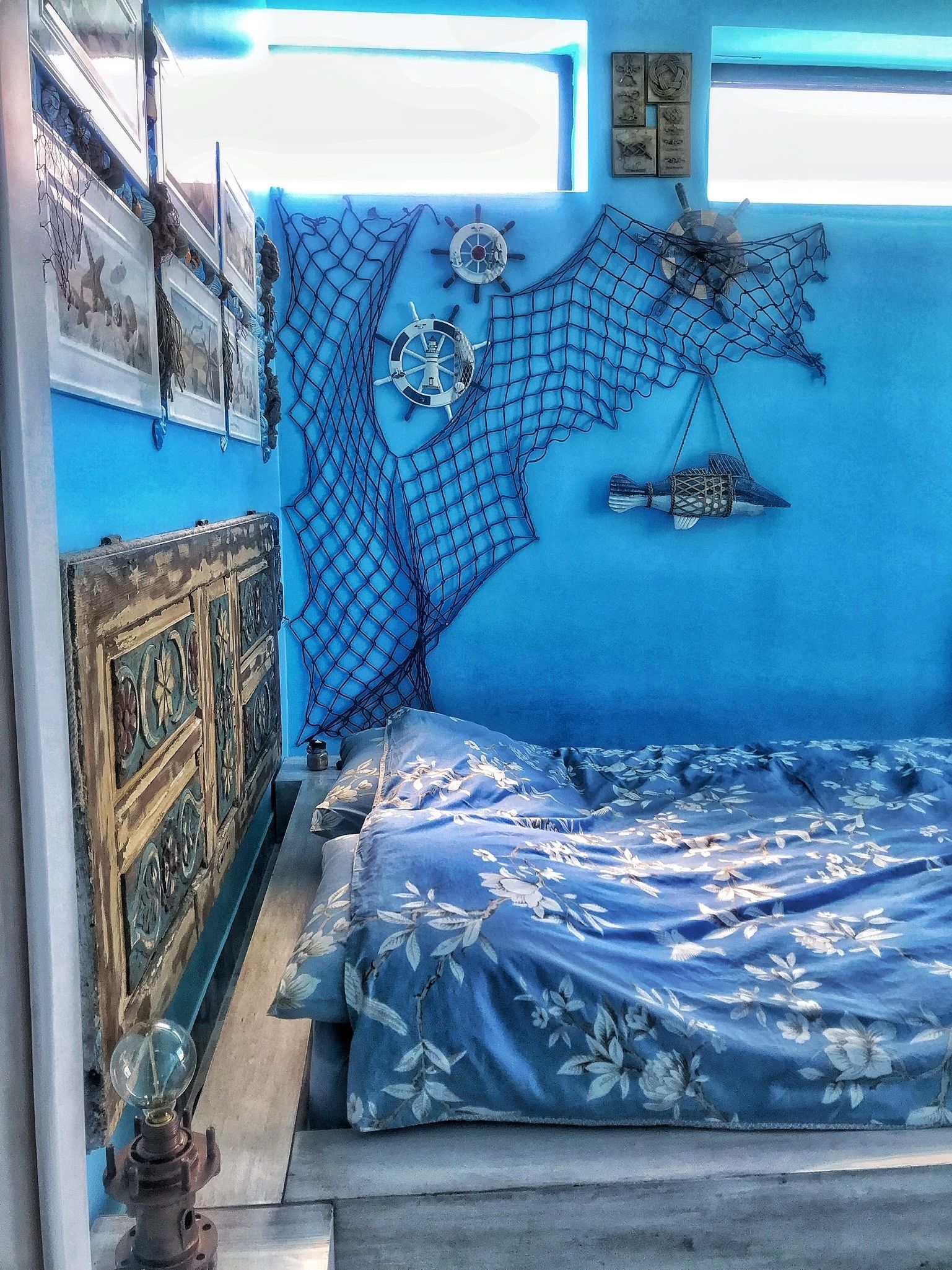 Una stanza con una parete blu, un letto con copriletto floreale, una testiera in legno e una ruota di timone a muro.
