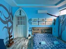 A bedroom with a nautical theme, featuring a bed with a blue and white pattern, a white door with a window, and wall decorations including framed pictures and a ship's wheel.