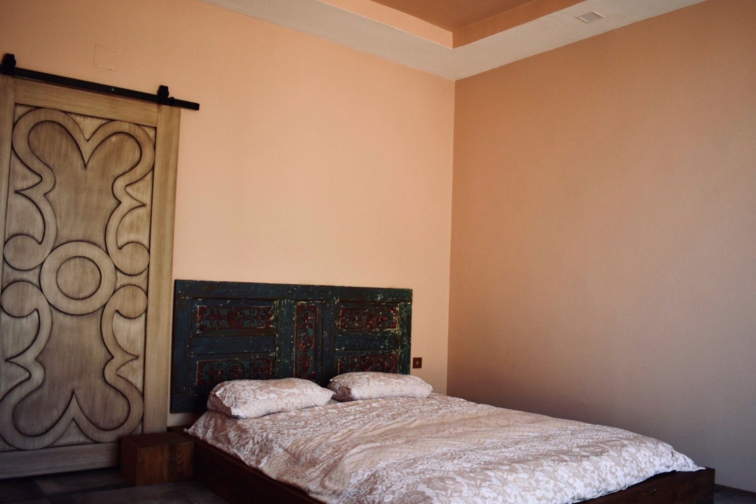A bedroom with a bed, a wooden wardrobe with decorative panels, and a plain wall.