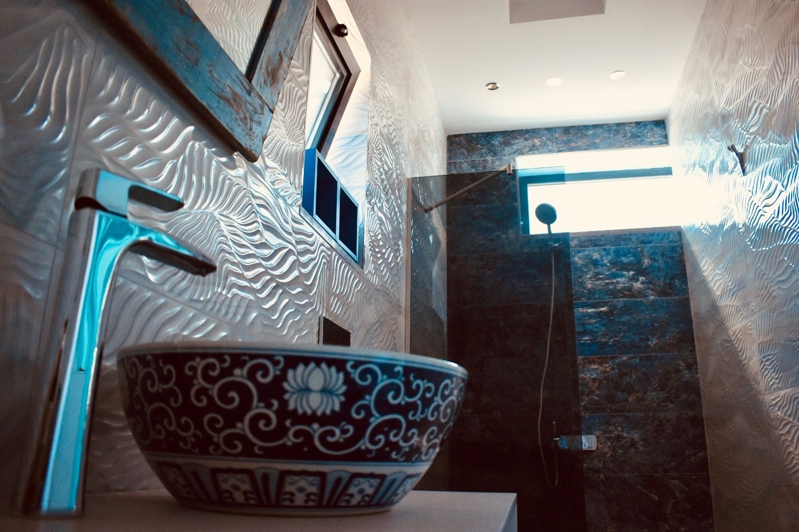 A bathroom with a decorative bowl on a counter, a shower area, and a view of the outdoors.