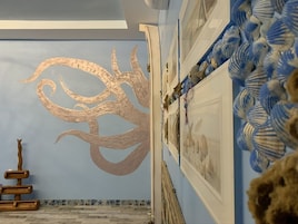 A room with a large abstract mural on the wall, a wooden sculpture, and a collection of blue and white striped objects on the right.