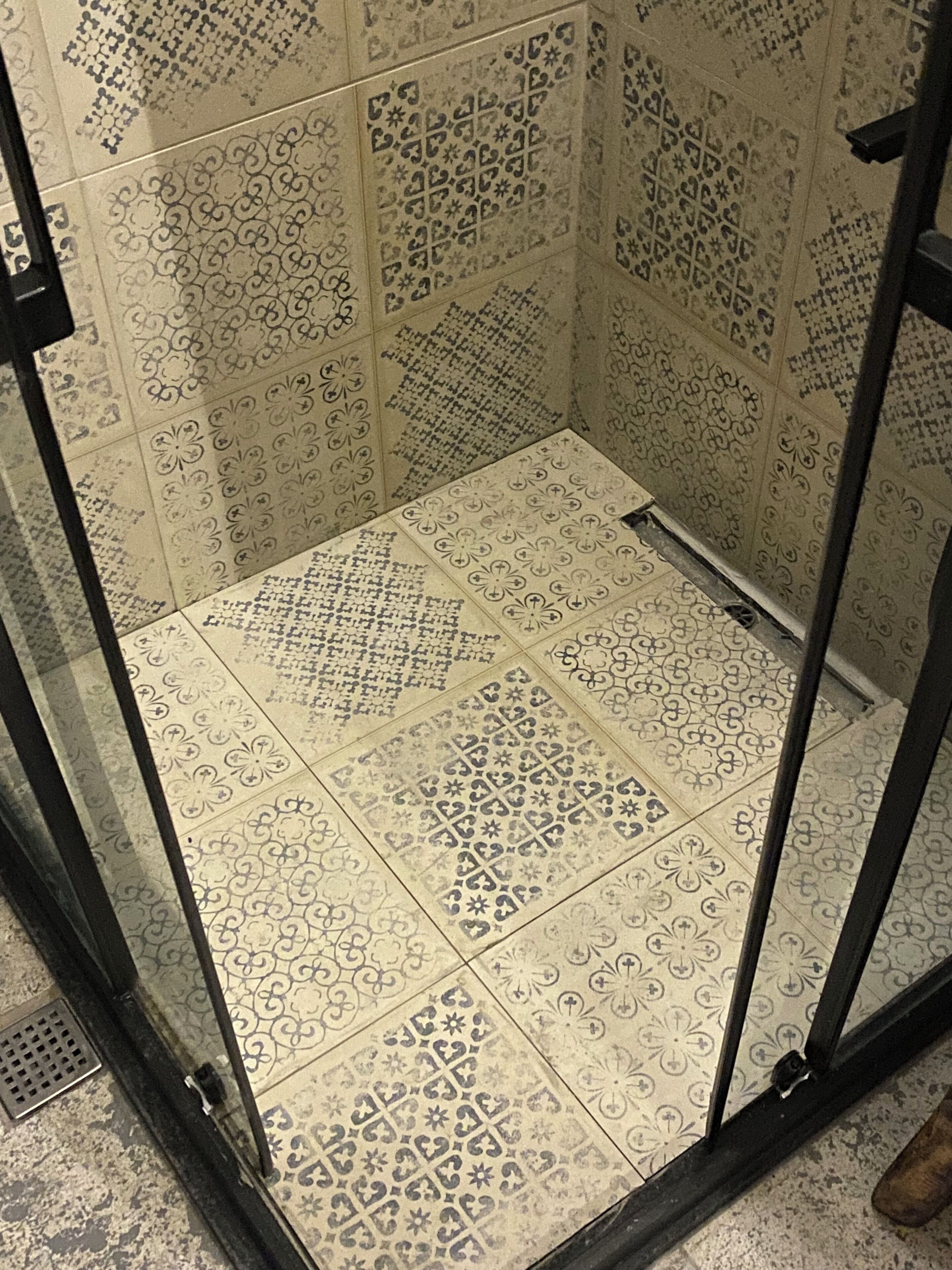 Un espacio de ducha con azulejos, puerta de cristal y marco de metal.