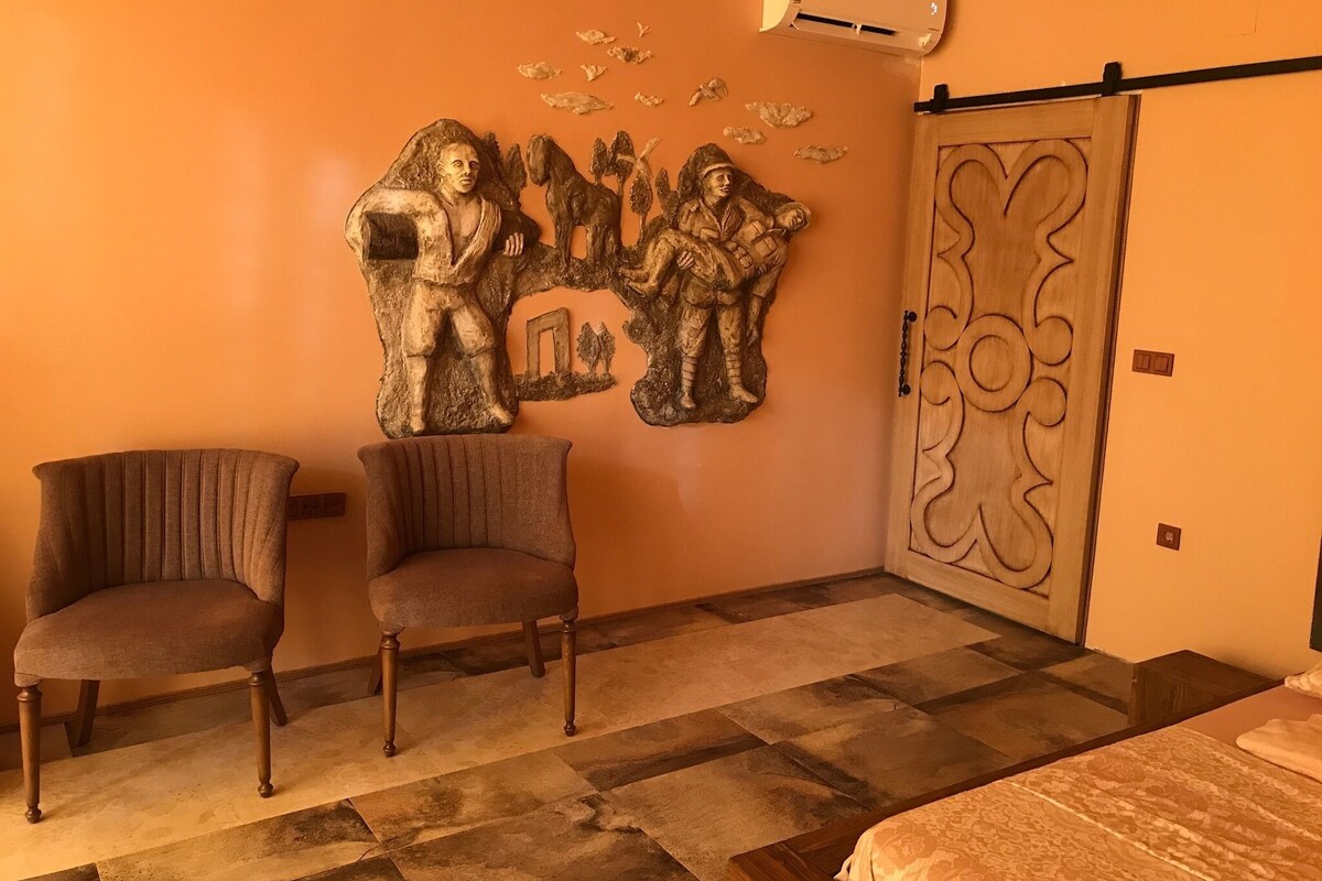 A room with a large wall sculpture, two armchairs, a bed, and a wooden door with a decorative design.