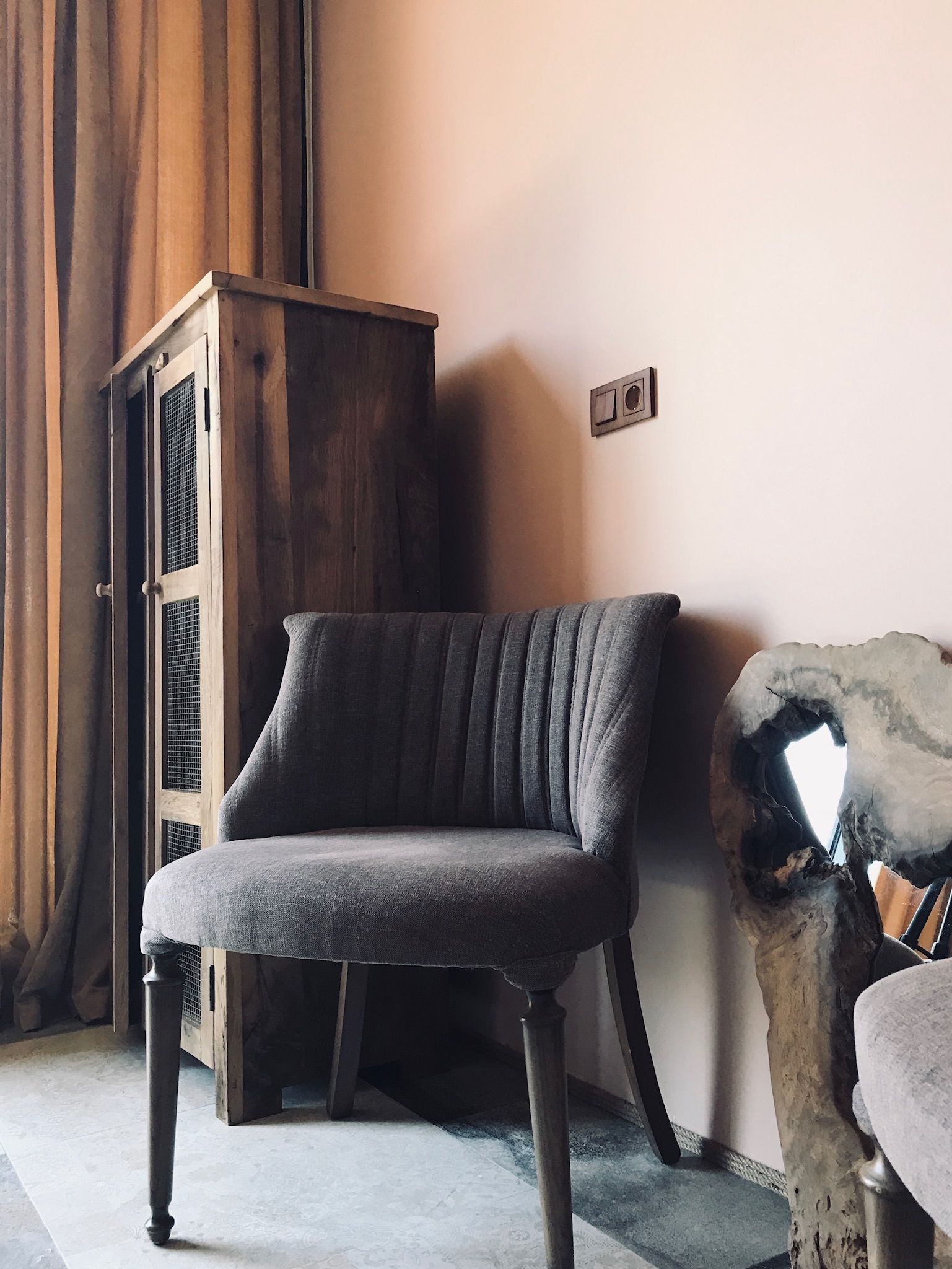 Una habitación de esquina con un aparador de madera oscura, un sillón tapizado en gris y una escultura de piedra.