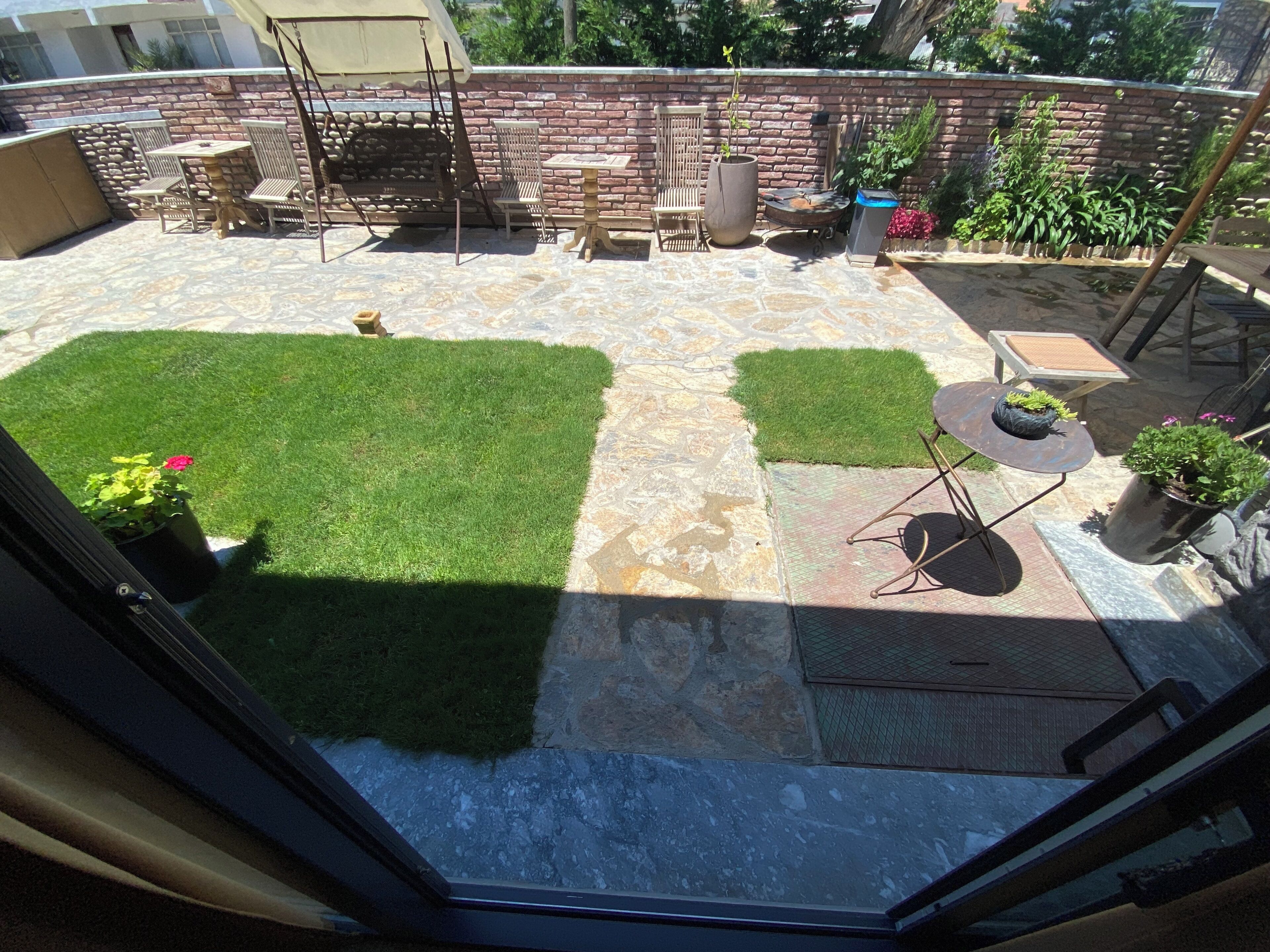 Un patio con piso de piedra, zona verde y mobiliario exterior.