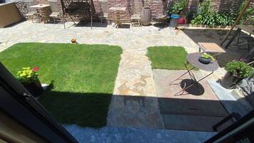 Un patio con piso de piedra, zona verde y mobiliario exterior.