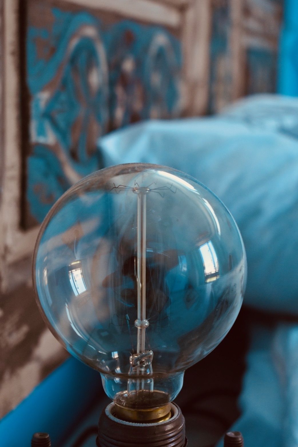 Une ampoule en verre transparent avec un socle en métal, placée sur un fond bleu orné de motifs abstraits.