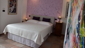 Ein Schlafzimmer mit einem großen Bett, zwei Nachttischen inklusive Lampen, einer violetten Wand und einem Gemälde an der Wand.
