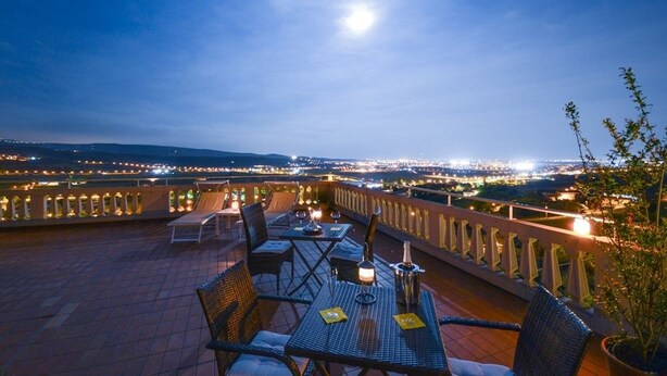 Eine Dachterrasse mit Tischen und Stühlen, Blick auf die Stadtlandschaft und ein Mond am Himmel.