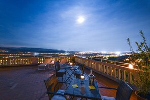 A rooftop terrace with tables and chairs, a view of the cityscape, and a moon in the sky. - B&B Ca Novecento (Verona)
