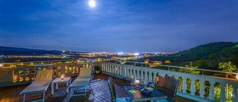 A terrace with outdoor seating and a view of a cityscape at night.
