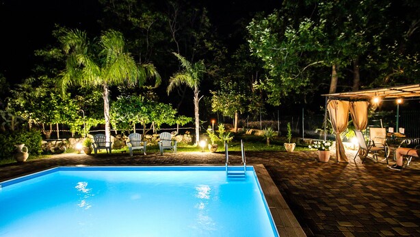 Ein Schwimmbad mit Liegestühlen und einer überdachten Sitzgelegenheit bei Nacht.